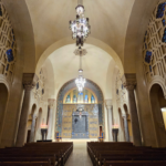 Grand Temple Emanu-El sanctuary with soaring arched ceilings, elegant stained glass, graceful chandeliers, and wooden pews.