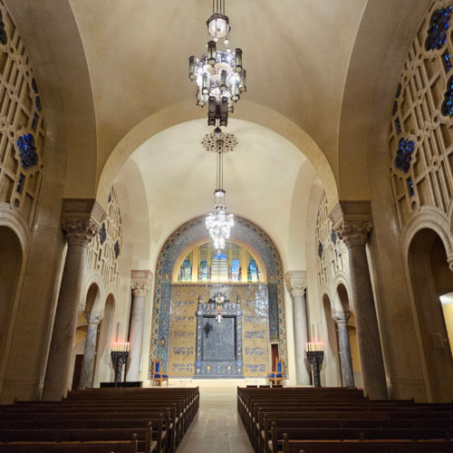 Grand Temple Emanu-El sanctuary with soaring arched ceilings, elegant stained glass, graceful chandeliers, and wooden pews.
