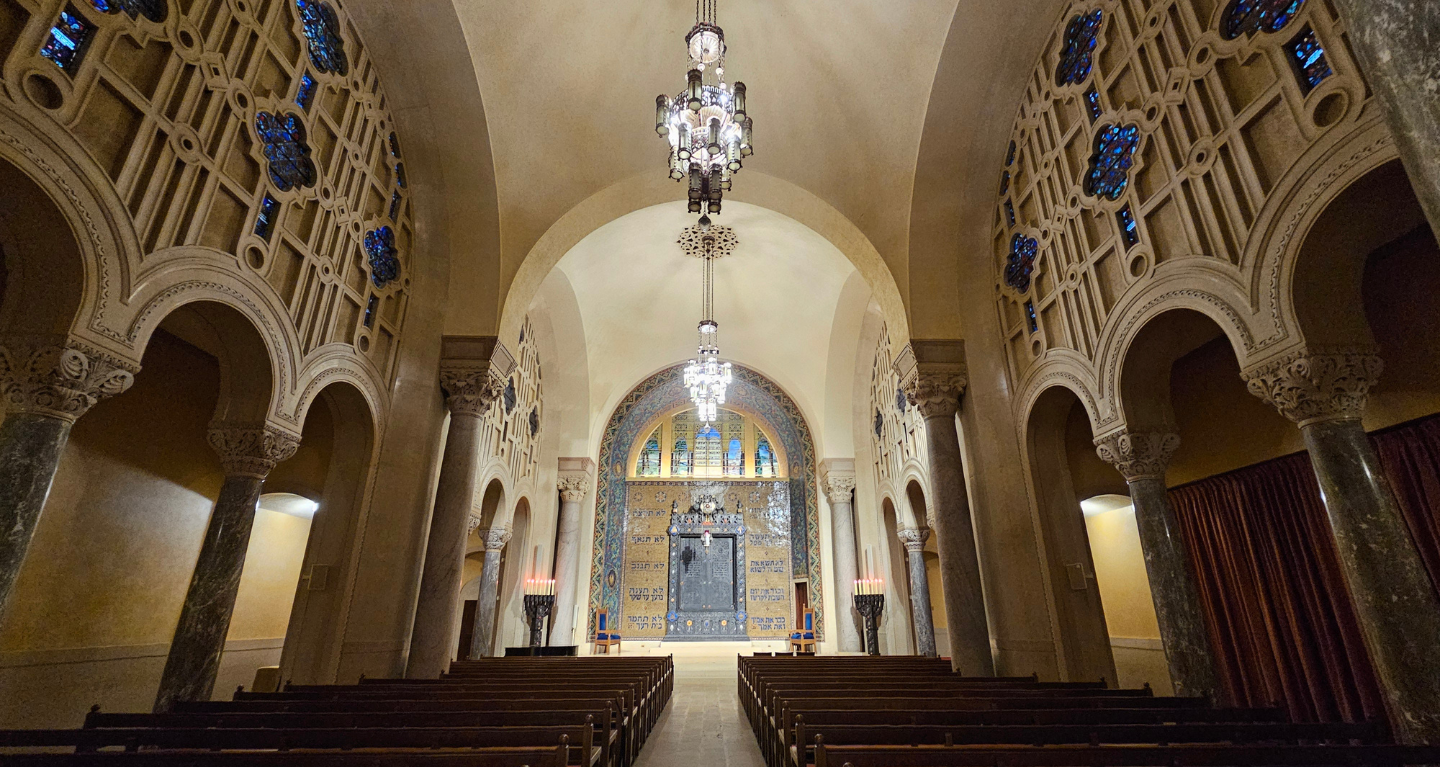 Grand Temple Emanu-El sanctuary with soaring arched ceilings, elegant stained glass, graceful chandeliers, and wooden pews.