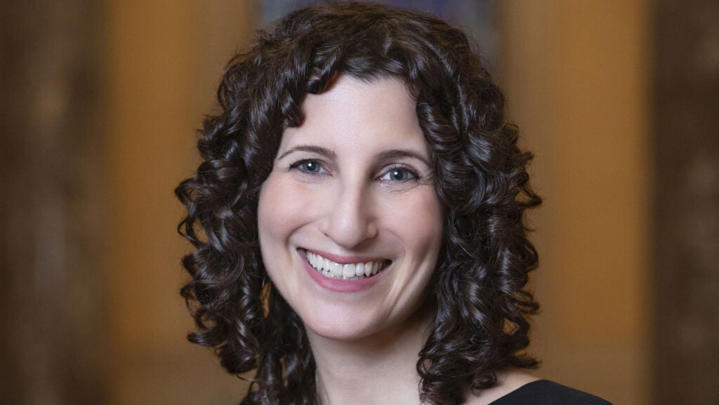 A portrait of a smiling woman with shoulder-length curly dark hair at Temple Emanu-El.