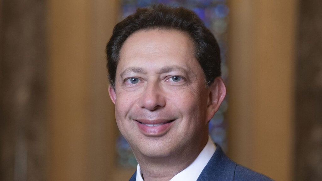 A professional headshot of a smiling man dressed in a suit, capturing a dignified and welcoming demeanor.