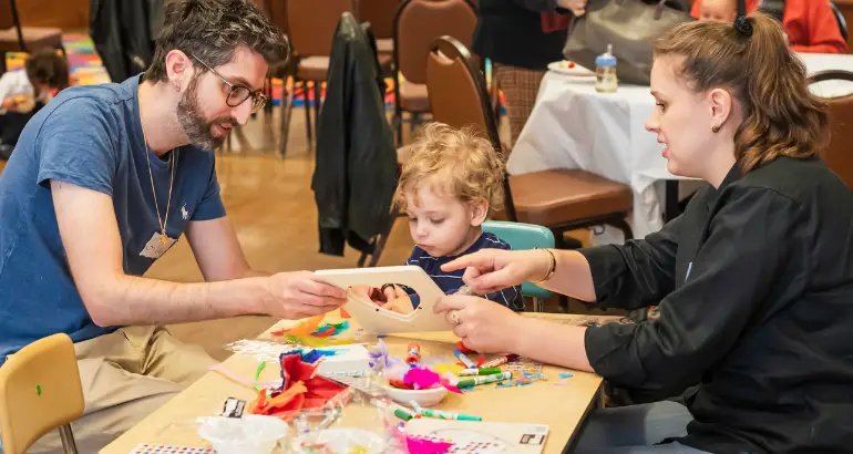 A family sits at a table in the temple, creating colorful arts and crafts together during a community event.