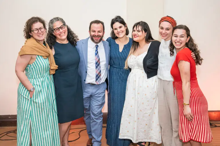 A group of seven of the administration and staff of Temple Emanu-El's Religious School standing together smiling with their arms over one another's shoulders.