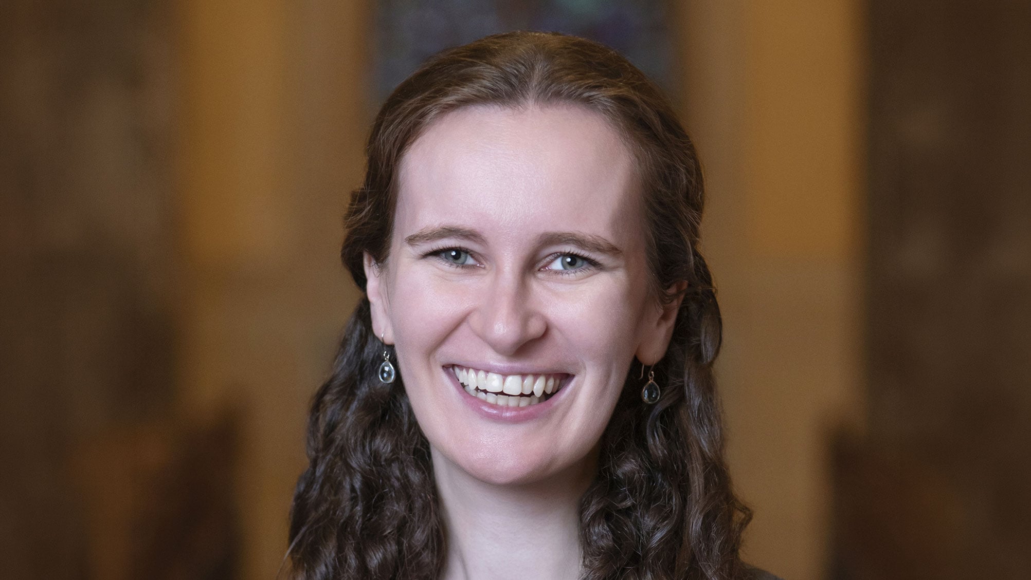 A smiling woman with long brown hair, captured in a portrait at Temple Emanu-El.