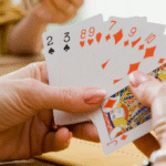 A person participates in a friendly card game at a table with others, holding a fan of playing cards.