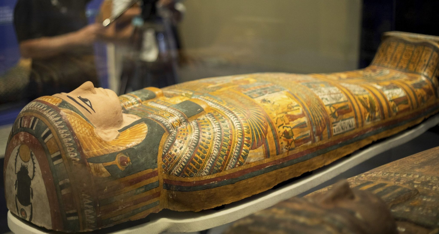 An intricately decorated ancient Egyptian sarcophagus exhibited in a respectful and educational setting.