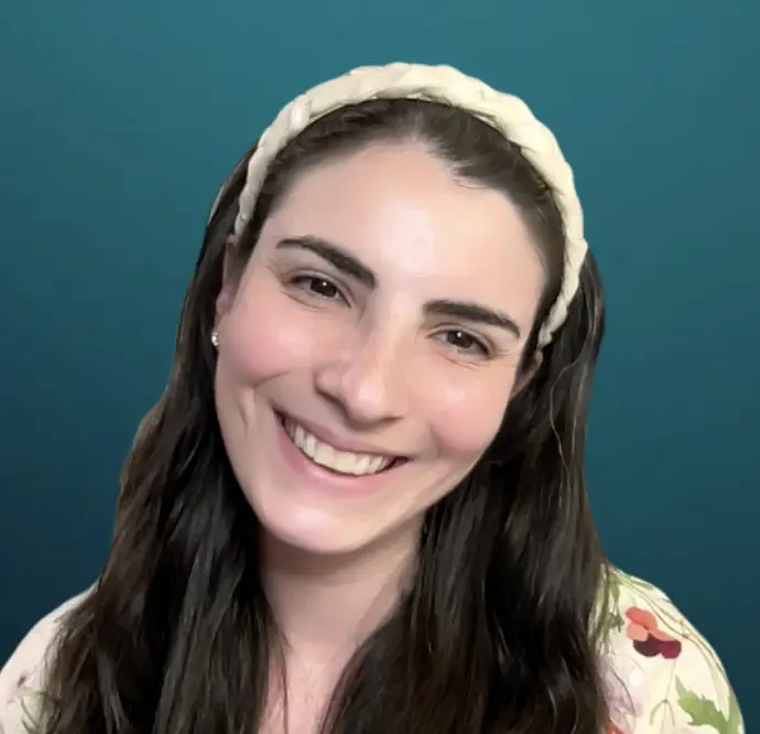 Smiling woman with long dark hair and a cream headband stands in front of a teal background at Temple Emanu-El, NYC.