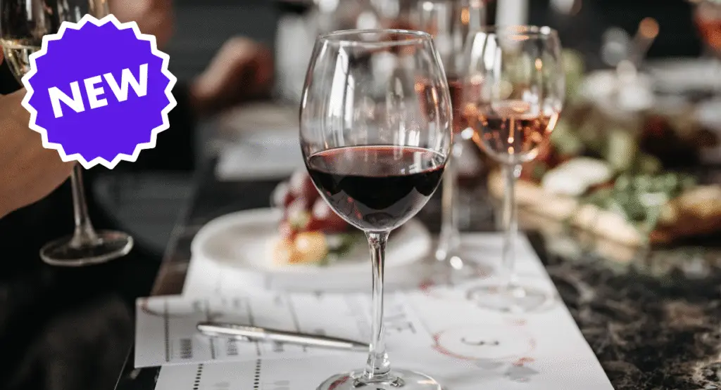 A glass of red wine on a table prepared for an event, with a NEW label in the top left corner.