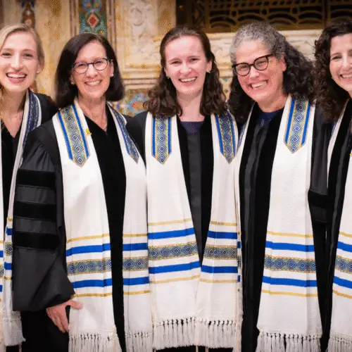 Five women in robes and white tallitot smile together inside Temple Emanu-El's sanctuary.