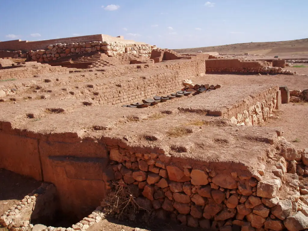 Ancient stone and mudbrick ruins from a historic site, set in a sunny, arid landscape beneath a clear blue sky.