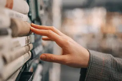 A hand reaching for books on a library shelf with blurred shelves in the background.