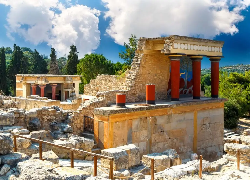 Historic stone columns and walls in a peaceful outdoor setting, shown under a partly cloudy sky with lush greenery around.