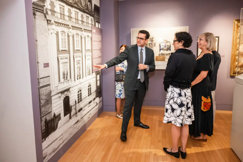 A man in a suit gestures toward a large black-and-white photograph as three women observe attentively in Temple Emanu-El's gallery.