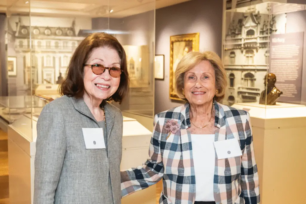 Two women, members of Temple Emanu-El, smiling together at a museum exhibit, both wearing name tags.