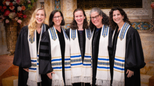 Five women in black robes and white tallitot smile together at Temple Emanu-El, gathered as a women's Jewish study group.