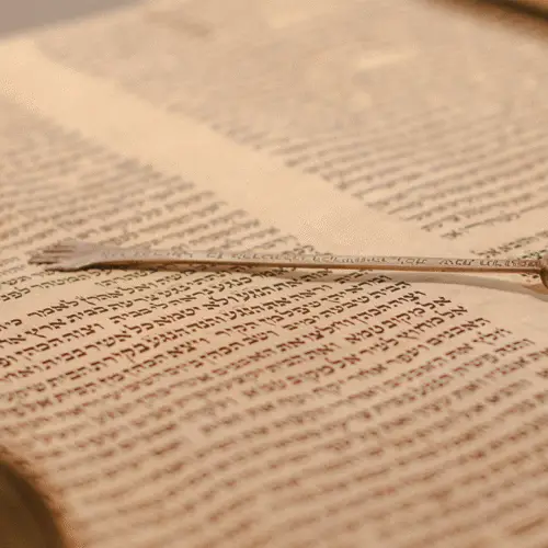 A silver yad pointer rests atop an open Torah scroll displaying handwritten Hebrew text at Temple Emanu-El in New York City.