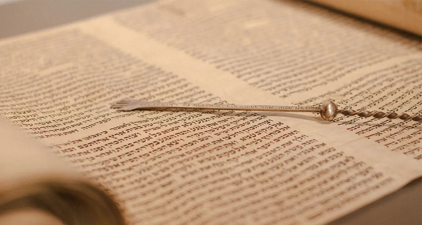 A silver yad pointer rests atop an open Torah scroll displaying handwritten Hebrew text at Temple Emanu-El in New York City.