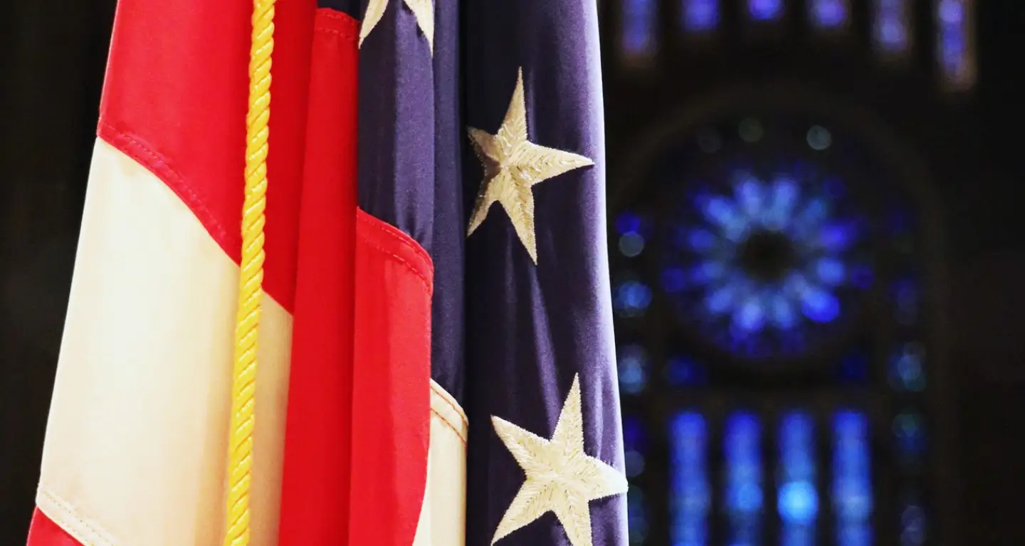 Close-up of an American flag next to a blurred stained-glass window inside Temple Emanu-El, New York City.