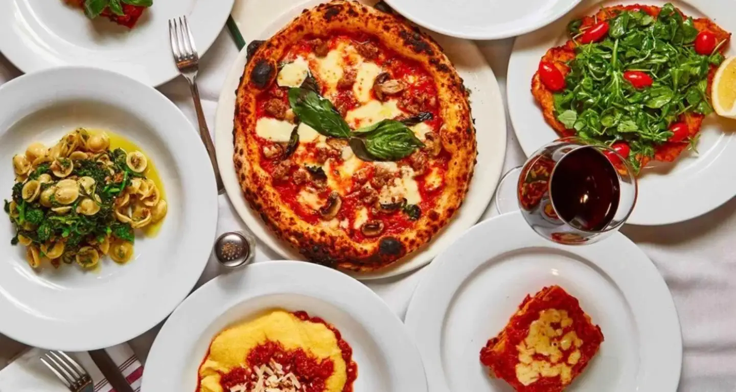 A table with pasta, salad, wine, and a variety of Italian vegetarian dishes on white plates.