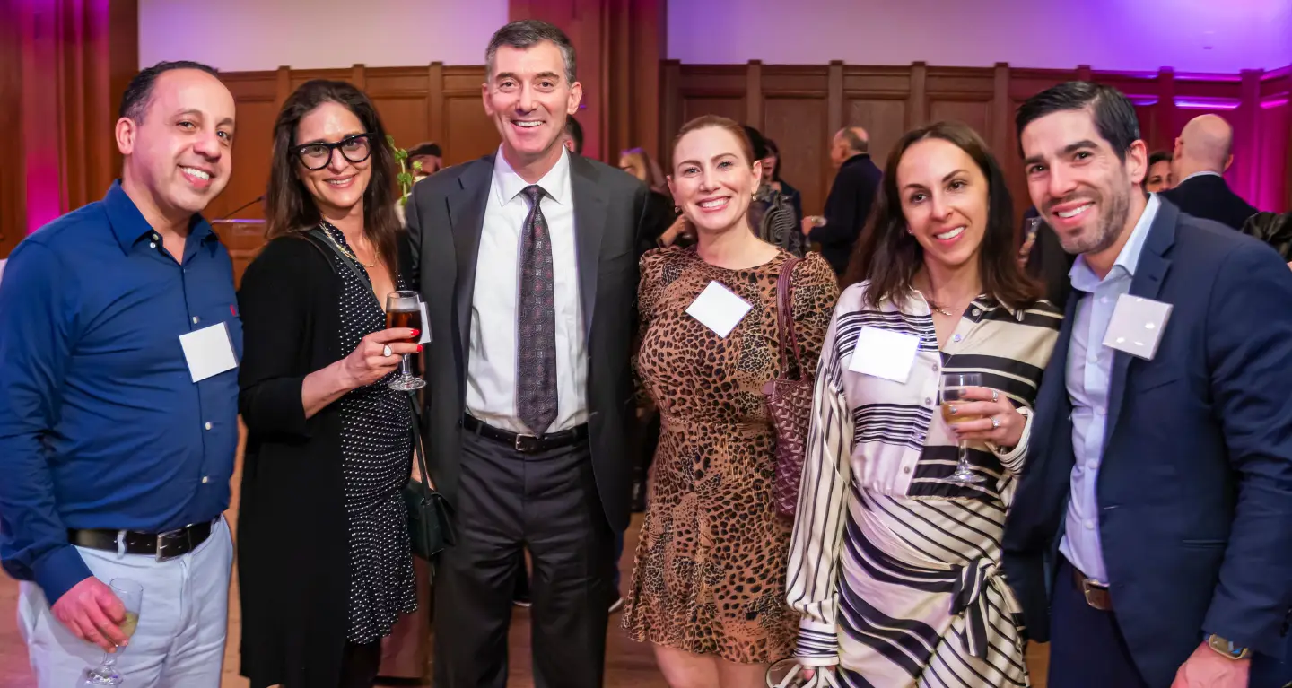 Six people in semi-formal attire smile as they pose together at a gathering inside Temple Emanu-El in New York City.