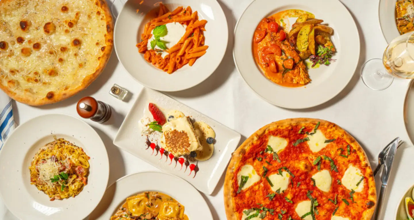 An overhead view of assorted Italian-inspired vegetarian dishes, pastas, and desserts on a white table at a synagogue event.