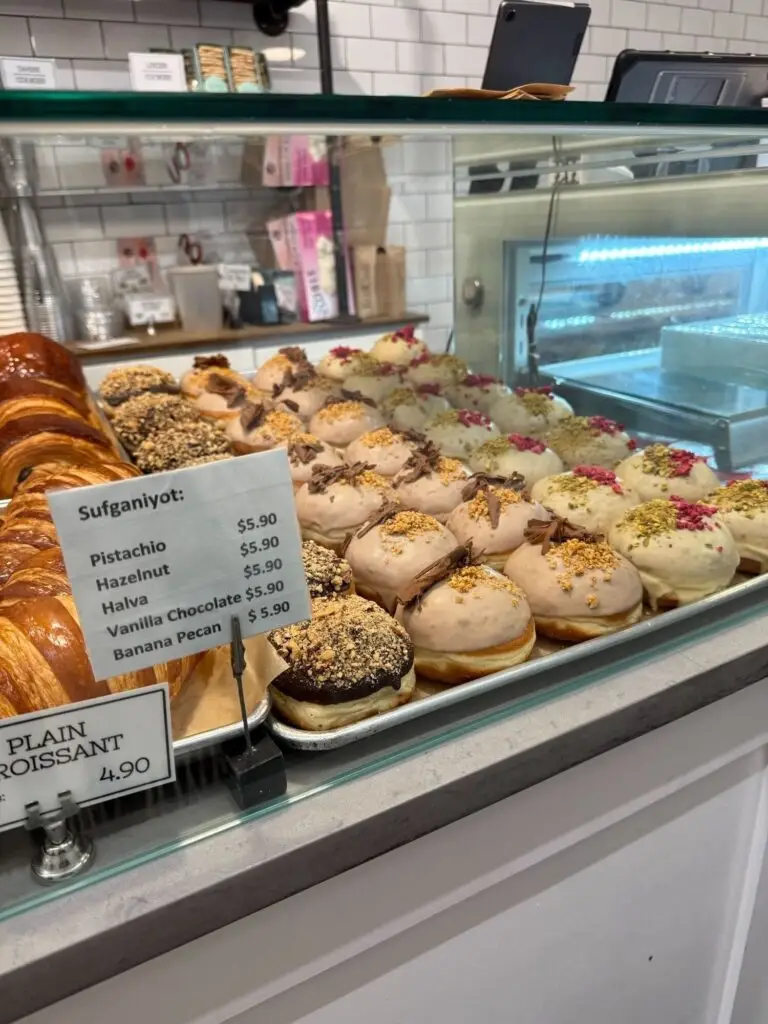 A display case featuring a variety of sufganiyot donuts on offer, with a sign detailing available flavors and prices.