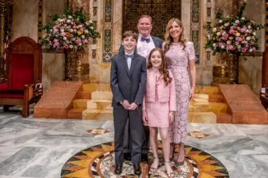Family of four dressed formally, smiling together in an elegant, flower-filled room at Temple Emanu-El in New York City.