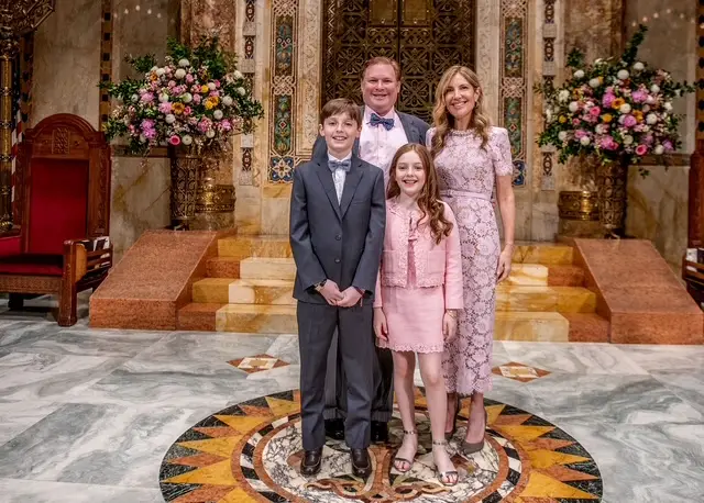 Family of four dressed formally, smiling together in an elegant, flower-filled room at Temple Emanu-El in New York City.