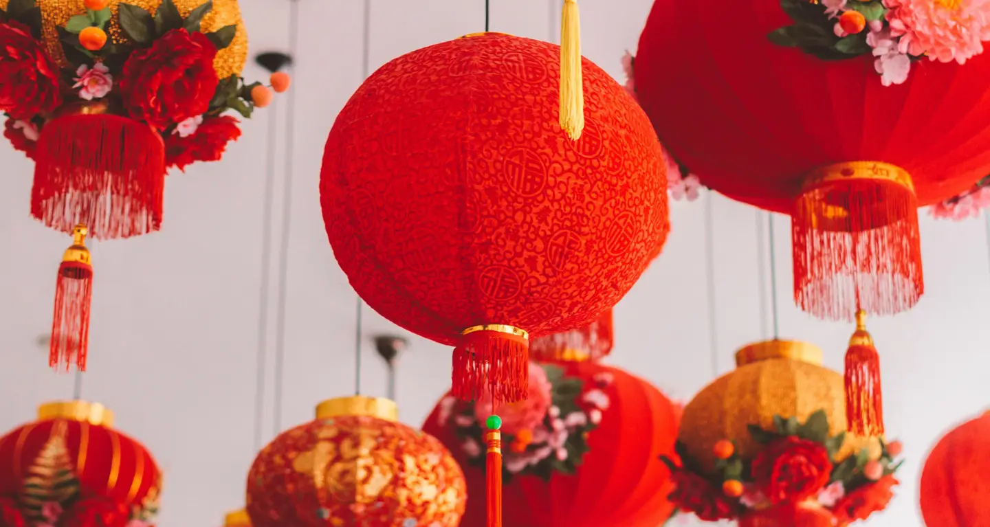 Red lanterns with decorative patterns and tassels hanging from the ceiling as festive decor for a multicultural celebration at Temple Emanu-El.