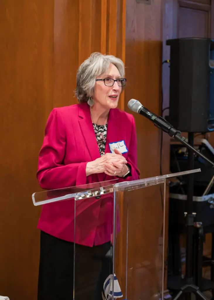 A woman in a pink blazer speaks at the podium with a microphone during an event at Temple Emanu-El in New York City.
