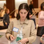 Temple Emanu-El members packing supplies into bags at a community service event, with tables and fellow volunteers in the background.