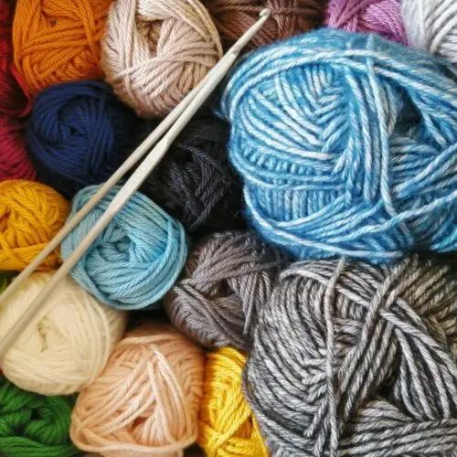 Colorful yarn balls with two knitting needles arranged on top.