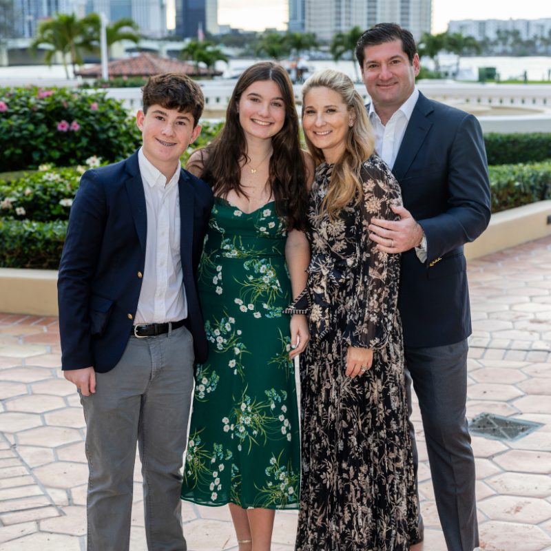 A family of four poses outside, dressed in semi-formal attire, with the city and greenery behind them.