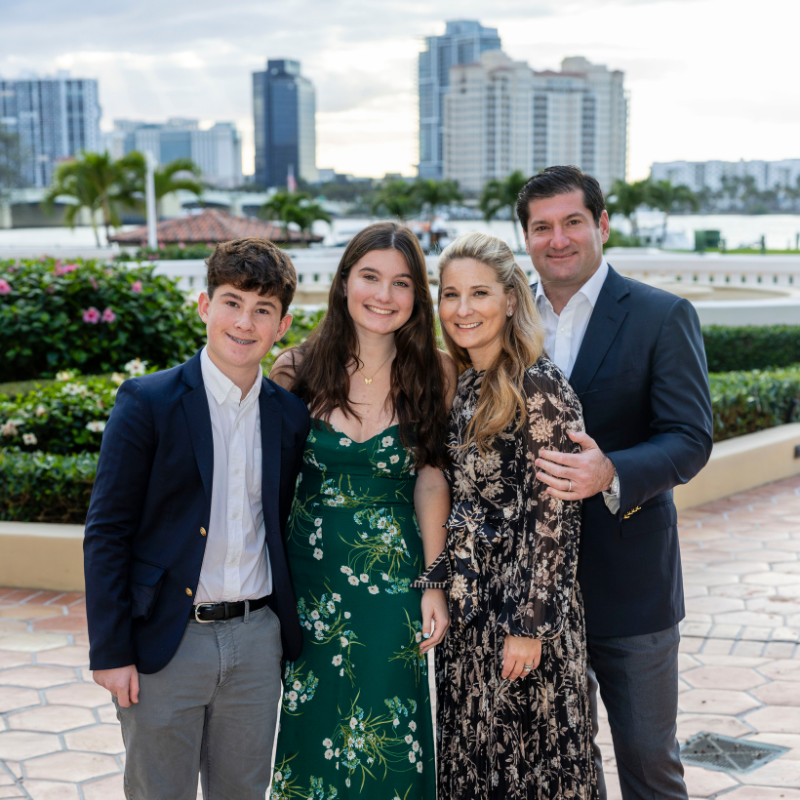 A family of four, dressed in formal attire, poses together outside.