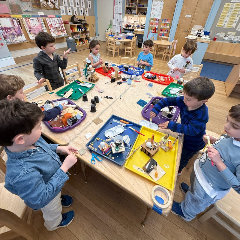 Eight children create arts and crafts together at a classroom table, surrounded by colorful supplies at Temple Emanu-El.