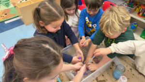Five young children play together with colorful water beads in a clear bin on a classroom table at Temple Emanu-El.