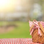 A picnic basket with a red and white checkered cloth on a matching tablecloth, set outside in the sun at Temple Emanu-El.