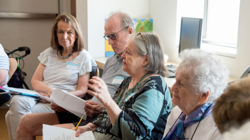 Four people sit in a circle holding papers and pencils, engaged in a lively group discussion.