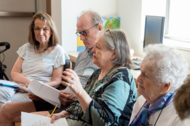 Four people sit in a circle holding papers and pencils, engaged in a lively group discussion.