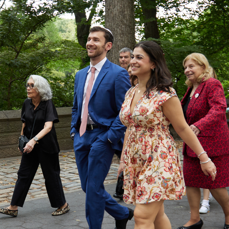 A joyful couple strolls with fellow congregants on a tree-lined path.