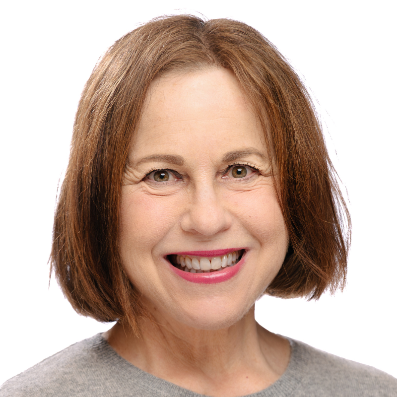 Smiling woman with straight brown hair wearing a modest grey top, photographed against a plain white background.