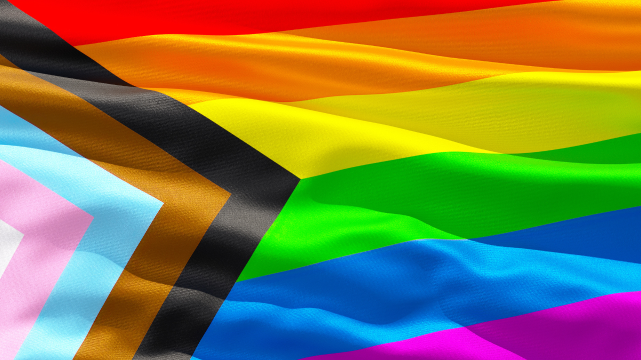 Progress Pride flag featuring rainbow stripes and chevron design on wavy fabric.