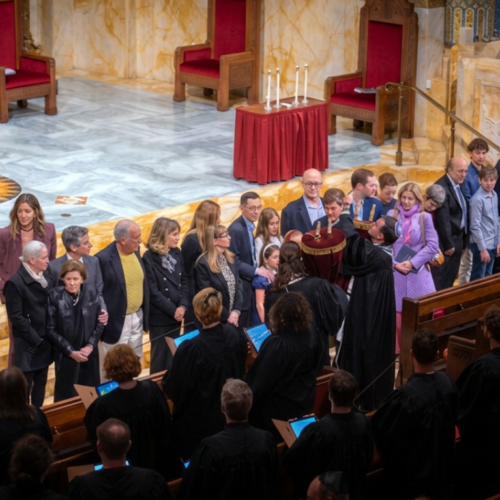 A group of people stands at the front of a sanctuary, facing clergy in robes during a ceremony at Temple Emanu-El.