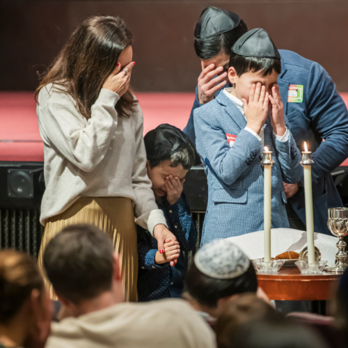 A family covers their eyes in prayer while lighting Shabbat candles at Temple Emanu-El in New York City.
