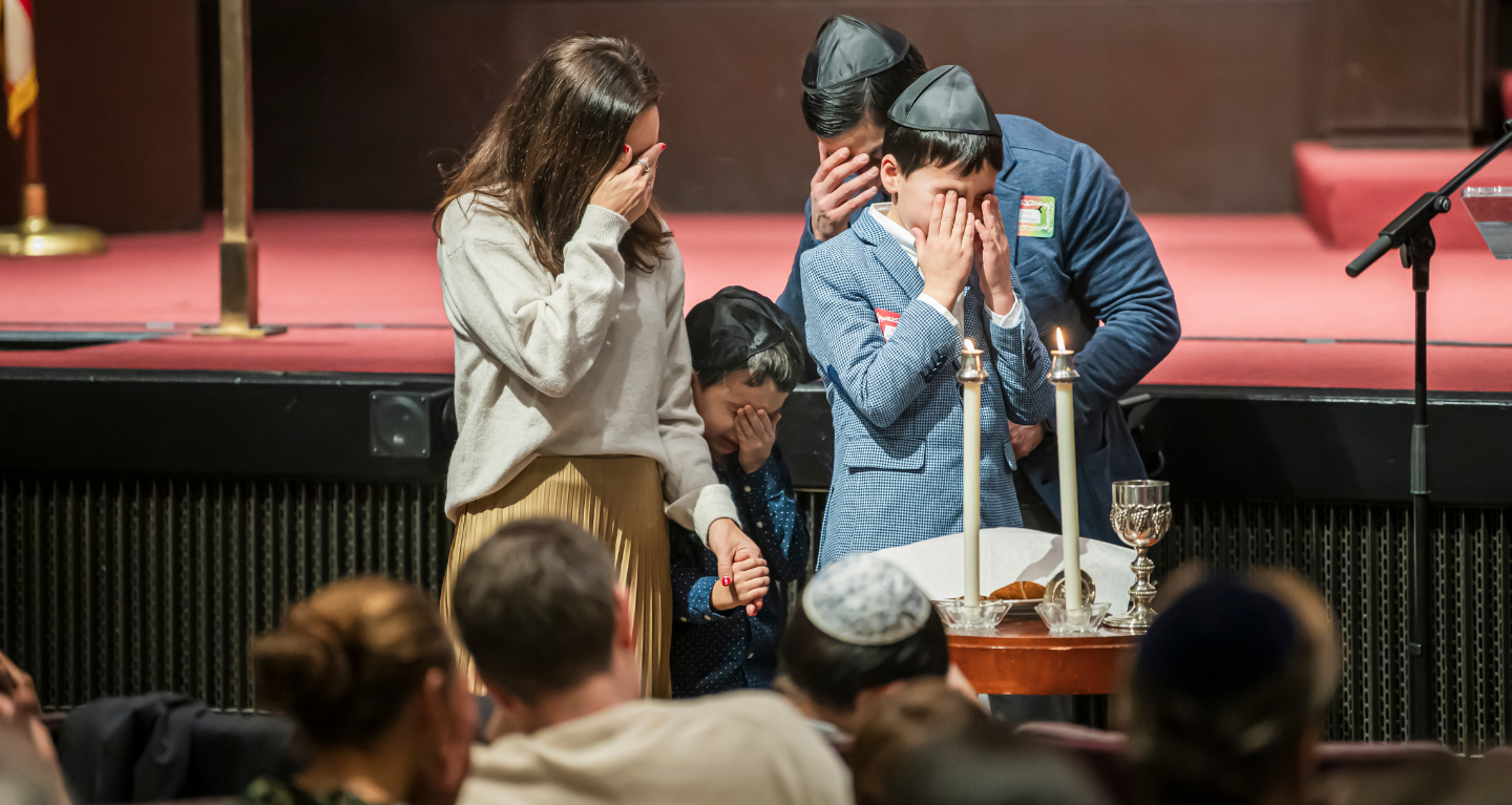 A family covers their eyes in prayer while lighting Shabbat candles at Temple Emanu-El in New York City.