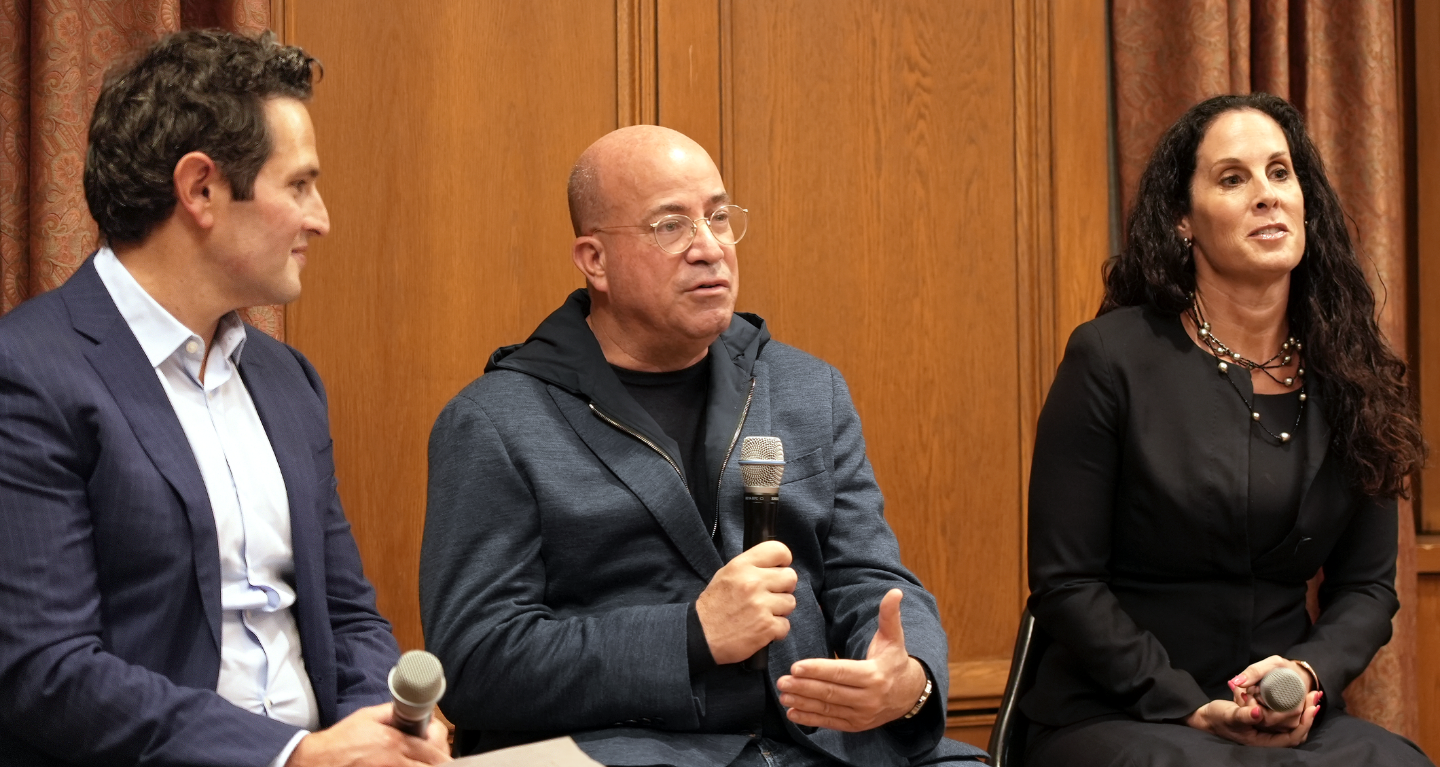Three individuals sit together in a welcoming indoor space at Temple Emanu-El; two men are holding microphones engaging in conversation, while a woman attentively listens.
