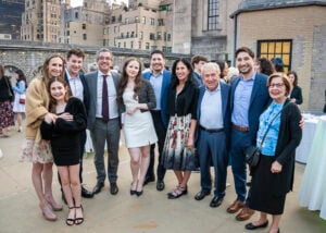 Formally dressed congregants smile together at an outdoor rooftop gathering overlooking the city at Temple Emanu-El.