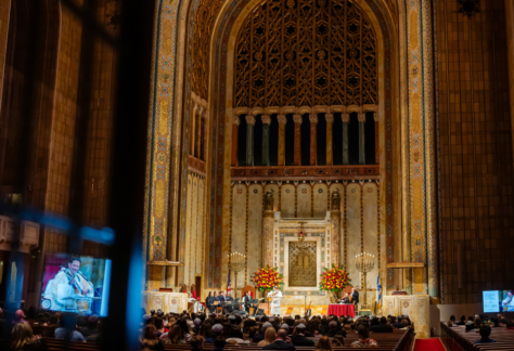 A large audience gathers for an event in the majestic sanctuary of Temple Emanu-El, surrounded by tall arches and elegant floral arrangements.