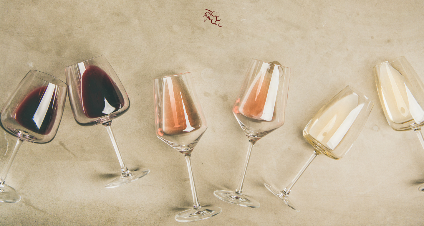 Five glasses, each filled with grape juice varieties in red, rosé, and white hues, tilted at gentle angles on a beige surface.