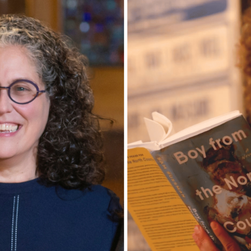 A smiling woman stands beside a man reading aloud from the book Boy from the North Country by Sam Sussman at Temple Emanu-El.